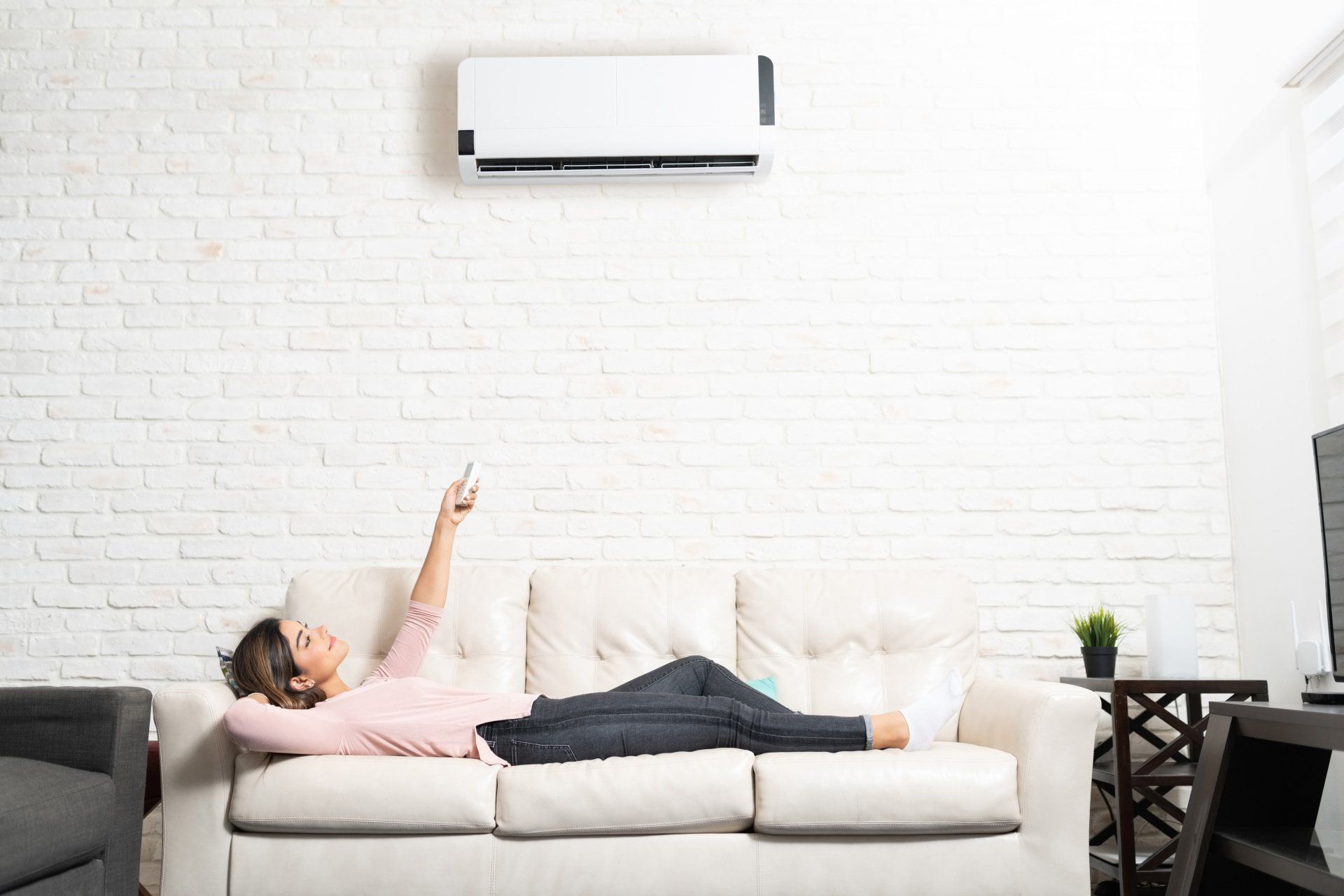 A woman is laying on a couch holding a remote control.