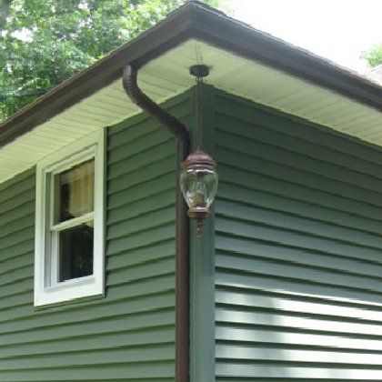 A green house with a gutter and a lamp on the side