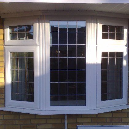 A white bay window with stained glass on a brick wall
