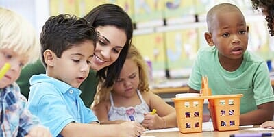 Teacher helping children in a classroom with their work; diverse group, focused expressions, bright colors.