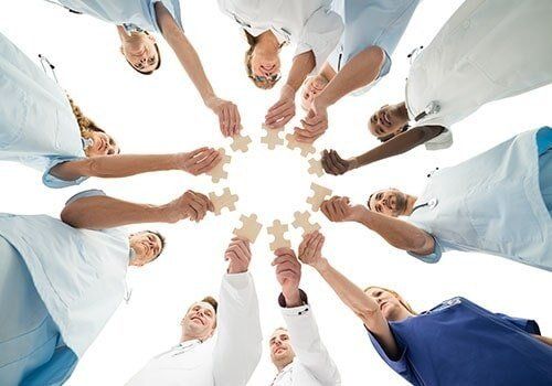 Medical professionals in circle holding puzzle pieces, collaborating.
