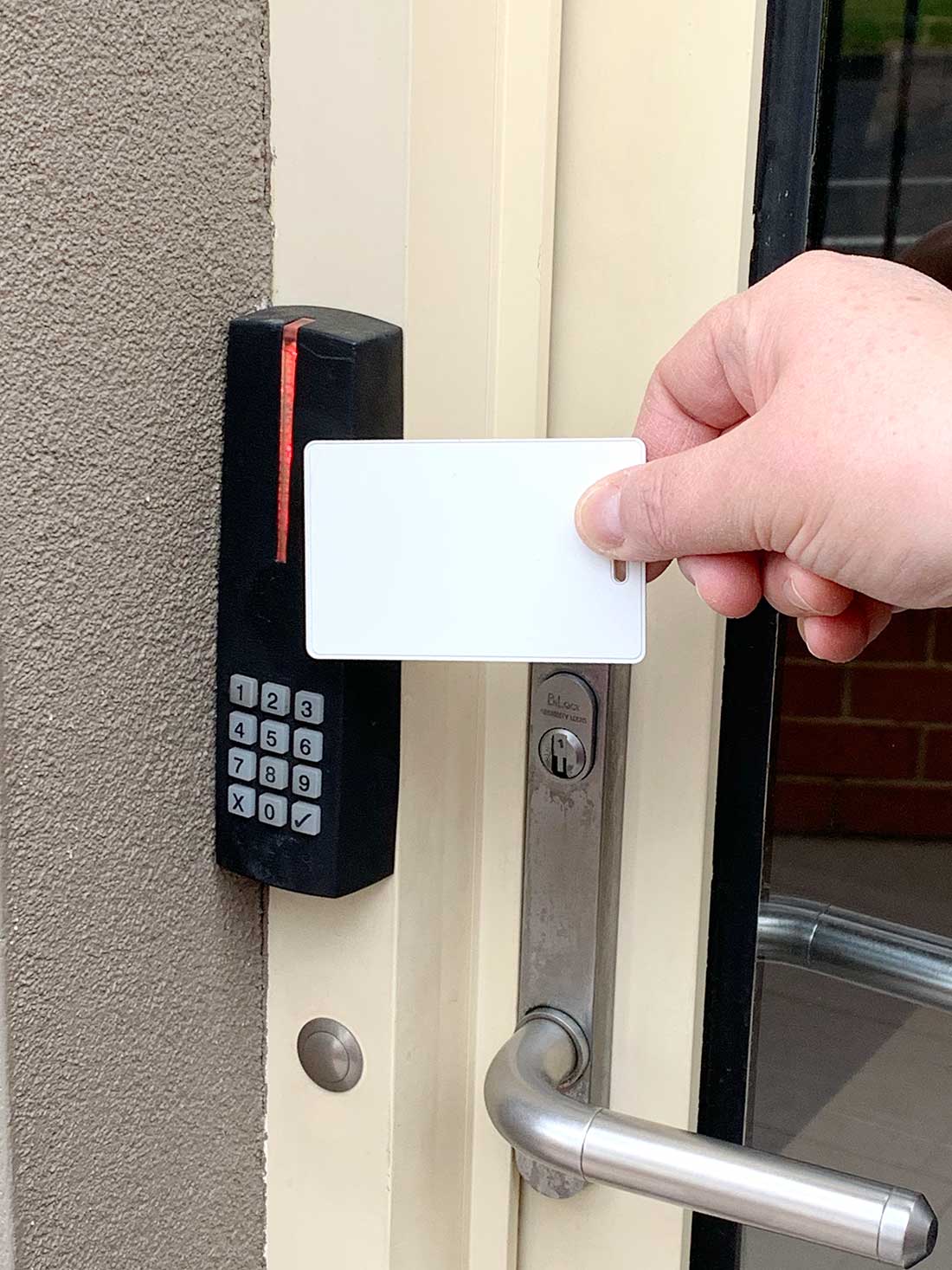 Hand holding a white card near a card reader and door handle to unlock door.