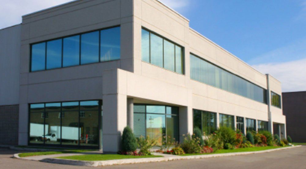 Modern two-story building with tinted windows; white and gray facade, green landscaping, blue sky.