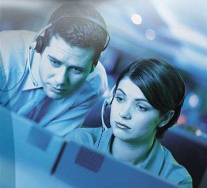 Two people with headsets, looking intently at a computer screen.