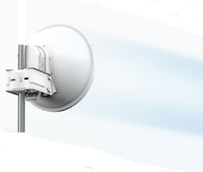 White parabolic antenna mounted on a pole, pointing right, against a light blue sky.