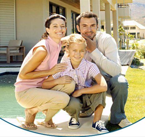 Family of three smiles outdoors near a pool and house.