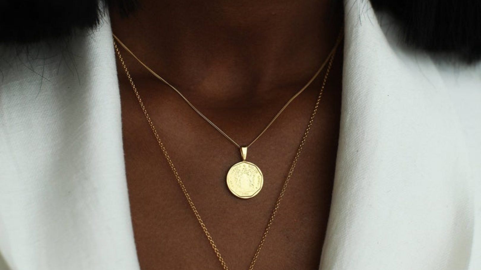 A woman is wearing a gold necklace with a coin pendant.