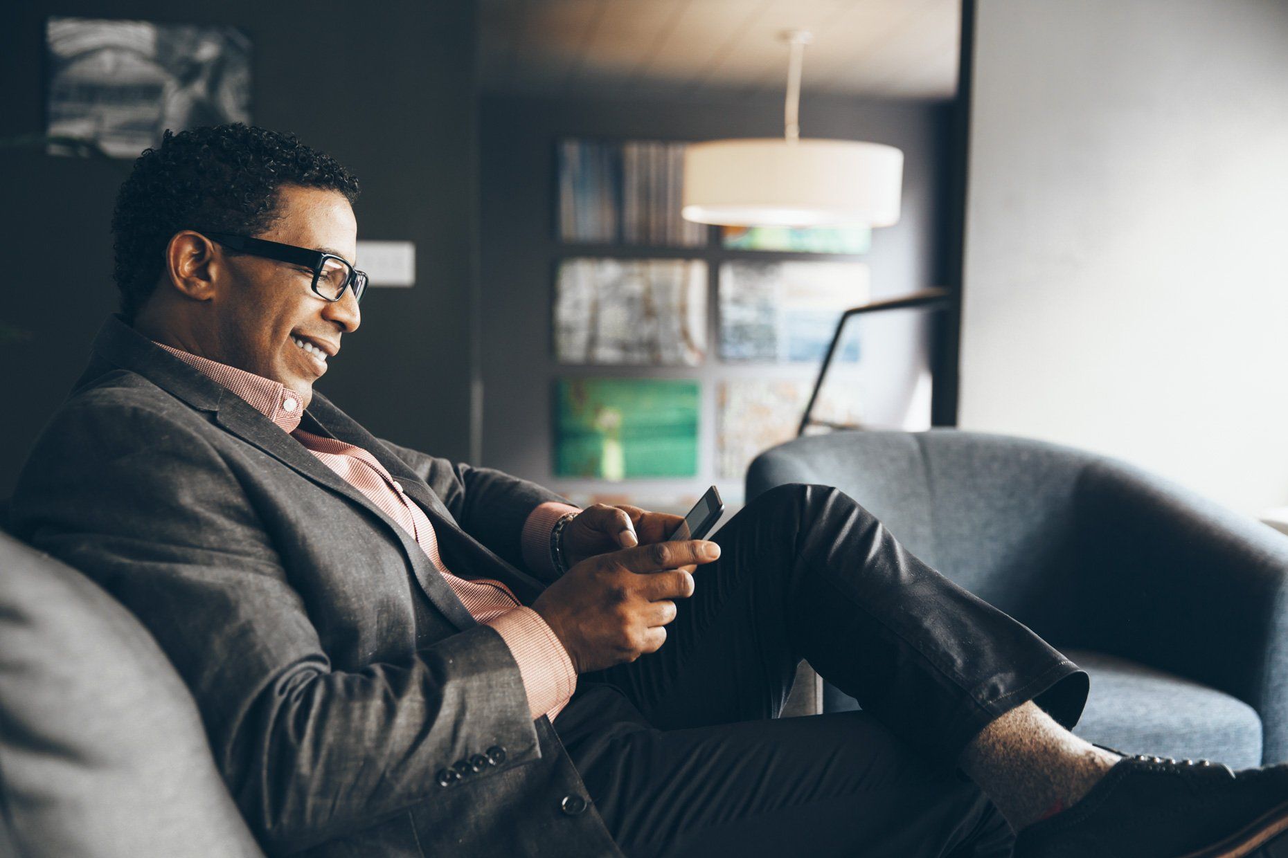 A man in a suit is sitting on a couch using a cell phone.