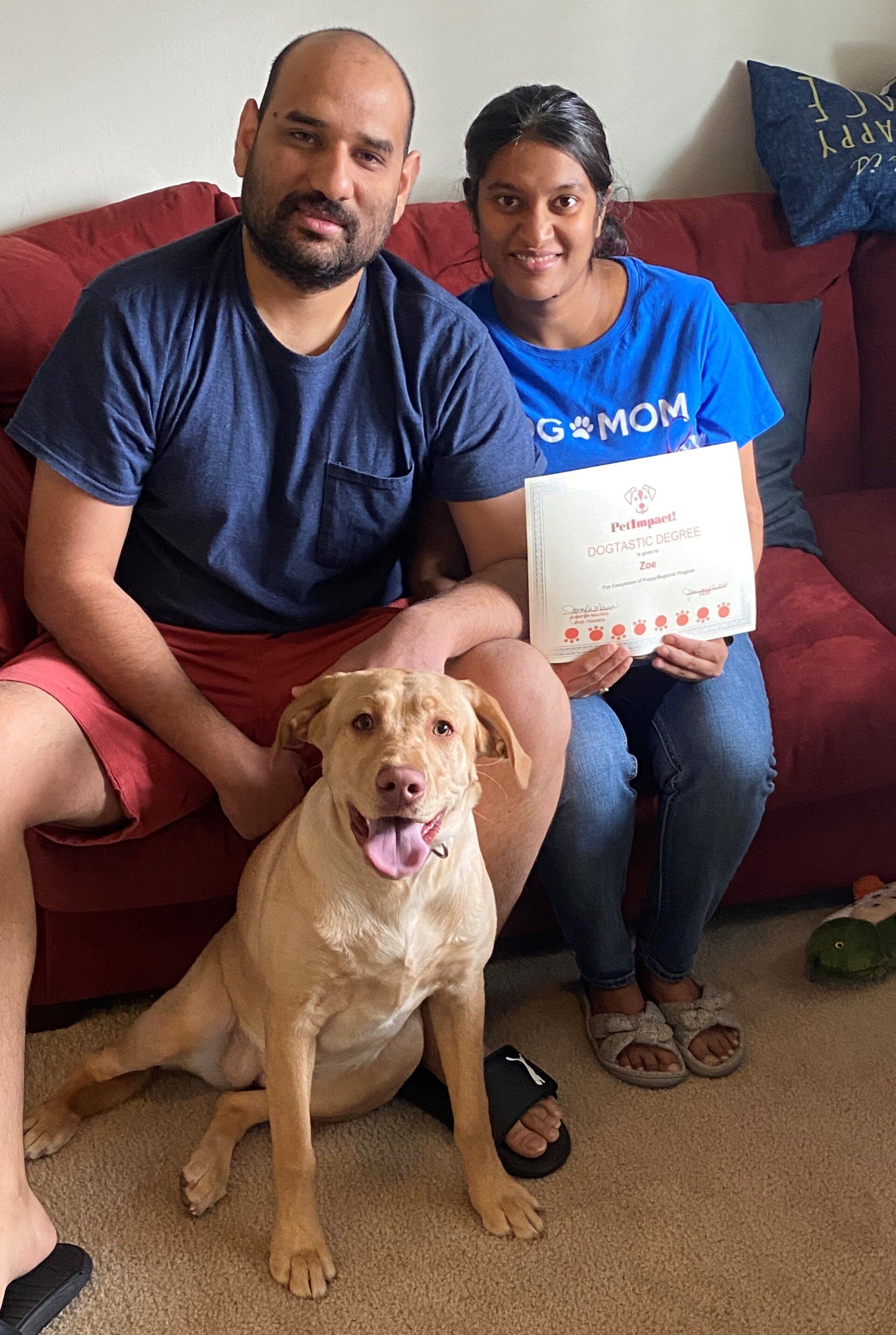 Couple with a dog, holding a certificate, sitting on a red couch.