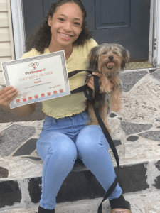 Girl holding certificate, smiling, with dog on leash. They are seated on steps.
