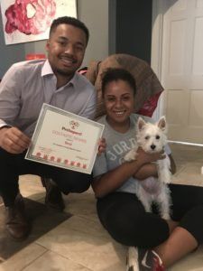 Man and woman holding an award and a small white dog, smiling.