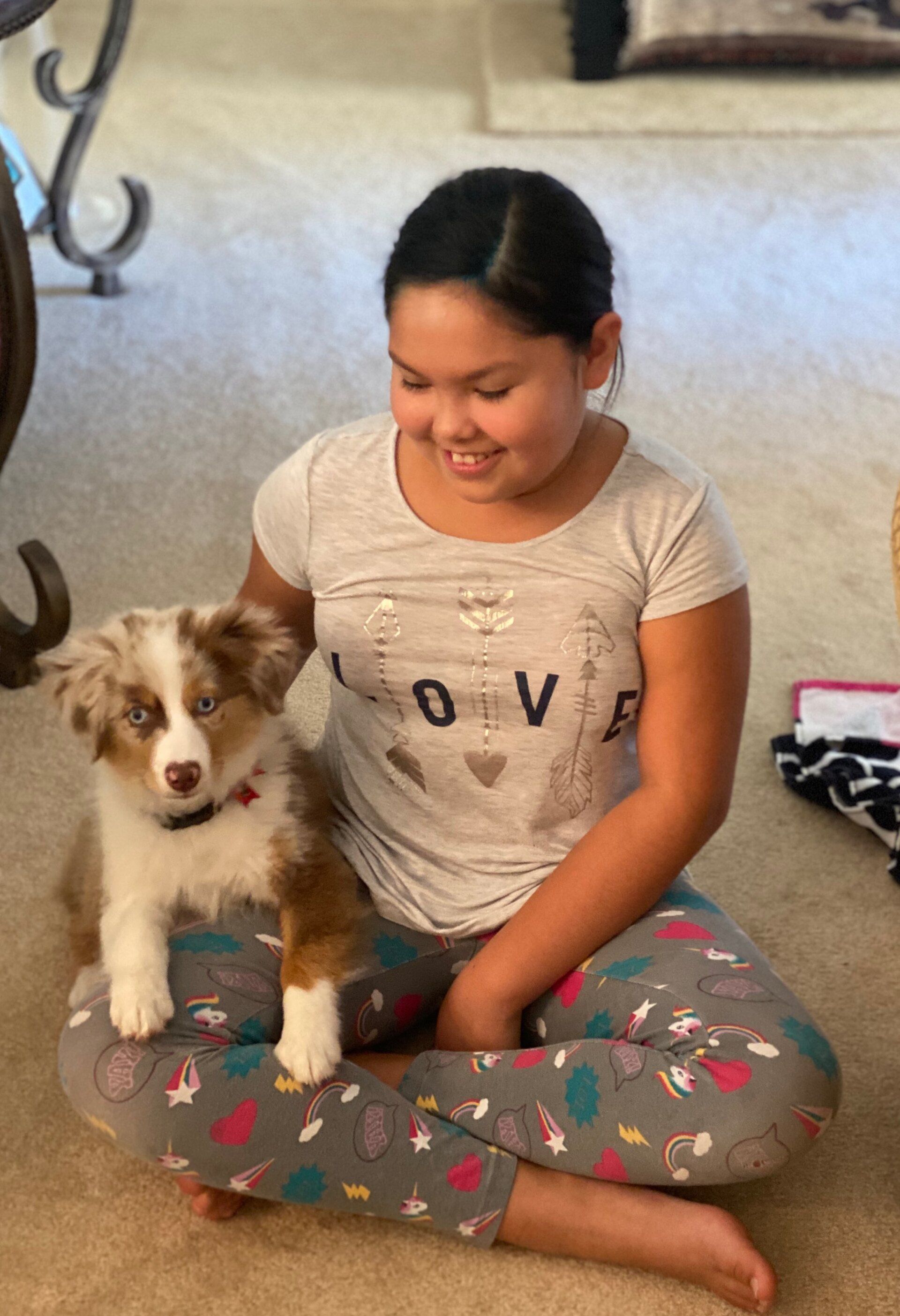 Girl sitting on floor with a brown and white puppy. Both are smiling.
