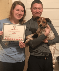 A couple holding a dog and a certificate, smiling. Certificate reads