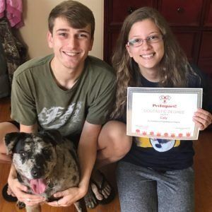 Two people and a dog; woman holds certificate.