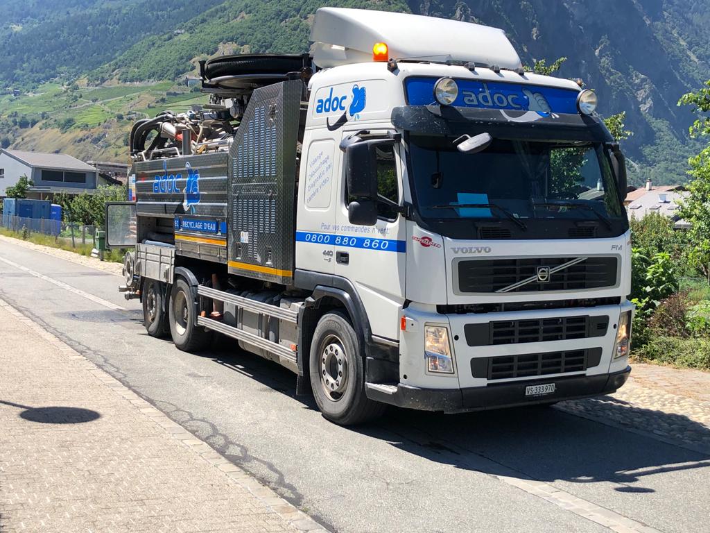 Un camion blanc roule sur une route avec des montagnes en arrière-plan.