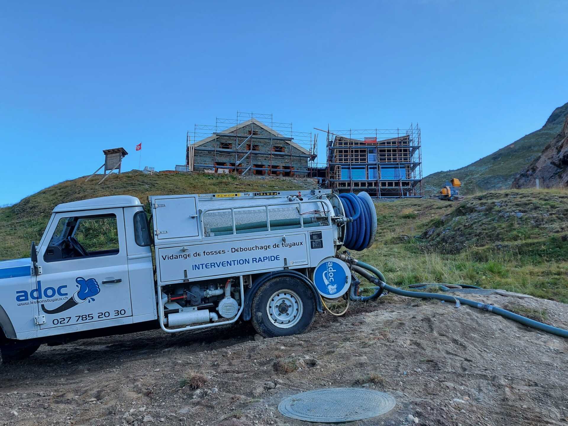 Un camion blanc avec un tuyau attaché est garé devant un bâtiment en construction.