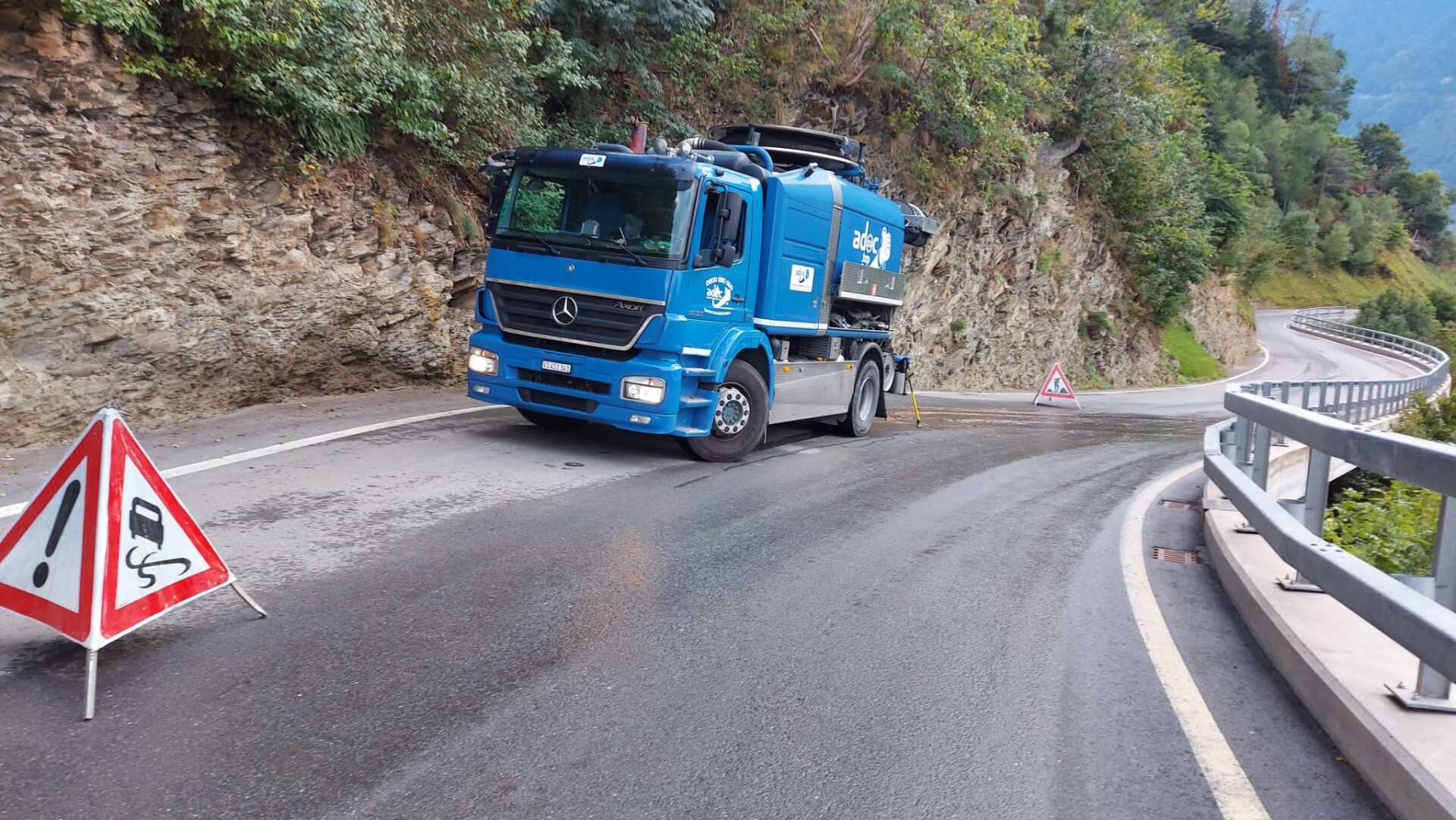 Un camion bleu roule sur une route sinueuse.