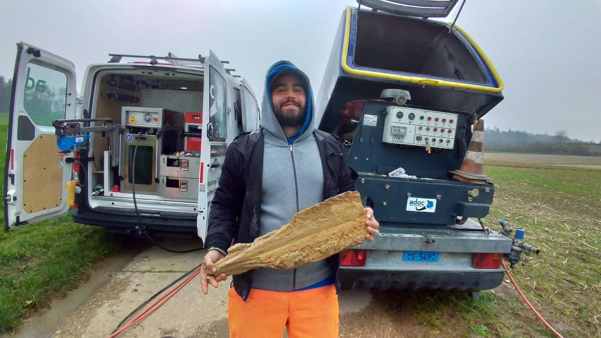 Un homme se tient devant une camionnette tenant un tuyau.