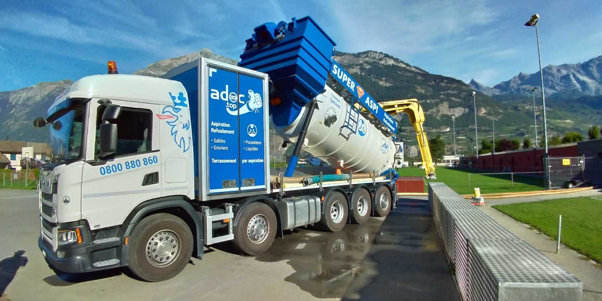 Un gros camion blanc et bleu est garé devant une montagne.