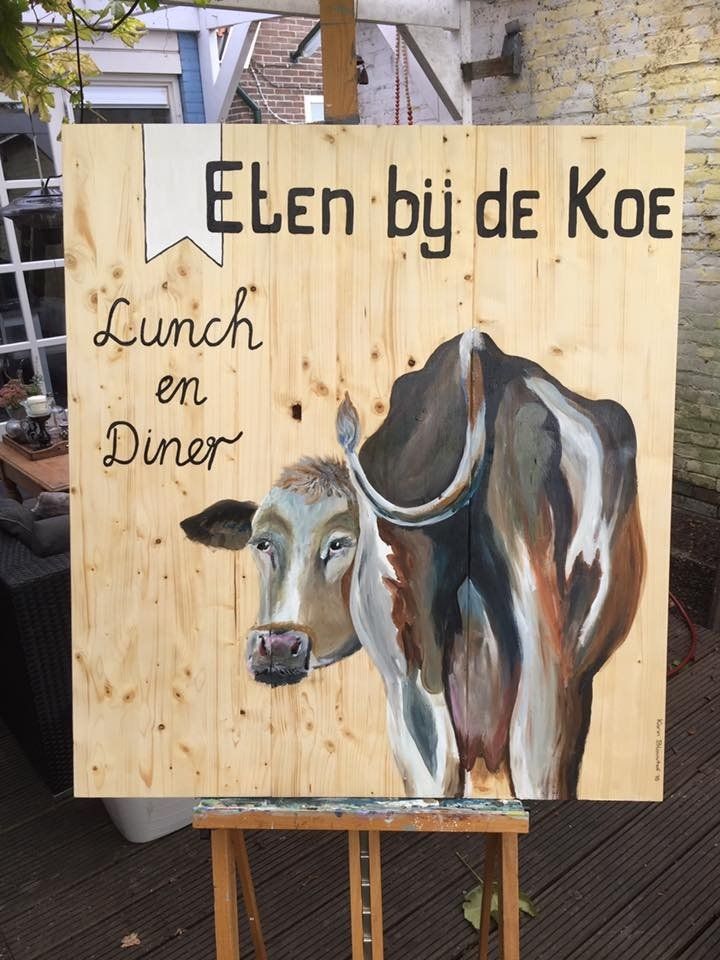 Houten bord met geschilderde koe en Nederlandse tekst: “Eten bij de Koe” en “Lunch en Diner”