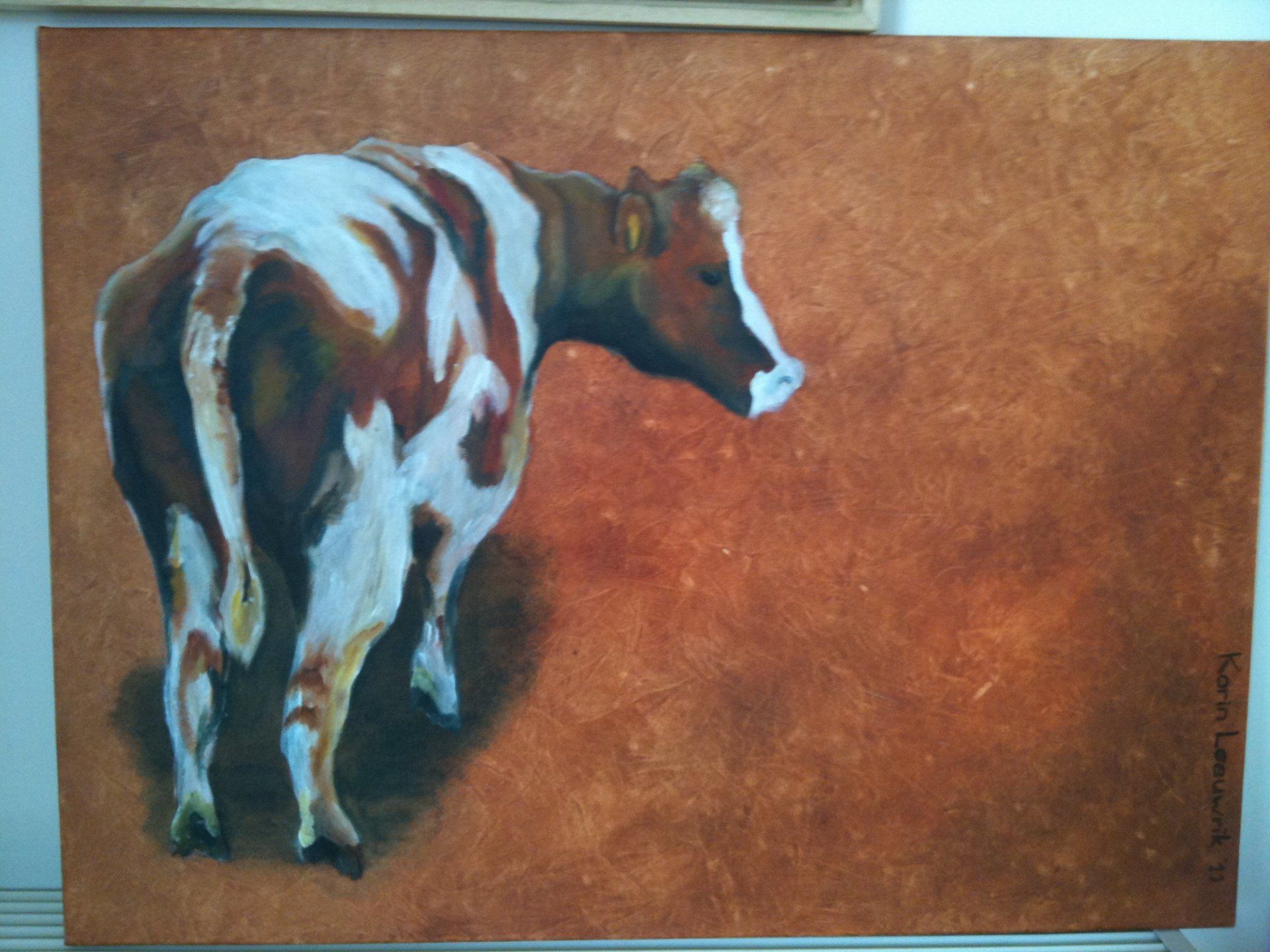 Geschilderde koe op een bruin canvas, van achteren gezien met een wit gezicht en donkerbruine vlekken.
