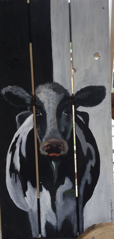 Zwart-wit schilderij van een koe op verweerde houten planken, met smalle openingen erdoorheen.