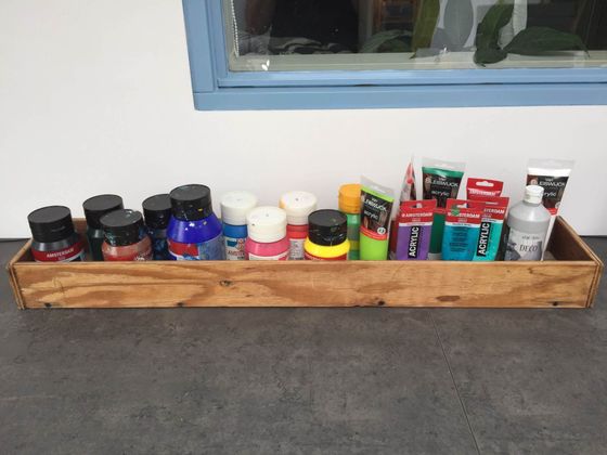 Een houten dienblad met diverse flessen, potten en kleine bakjes op een donker aanrecht onder een raam.