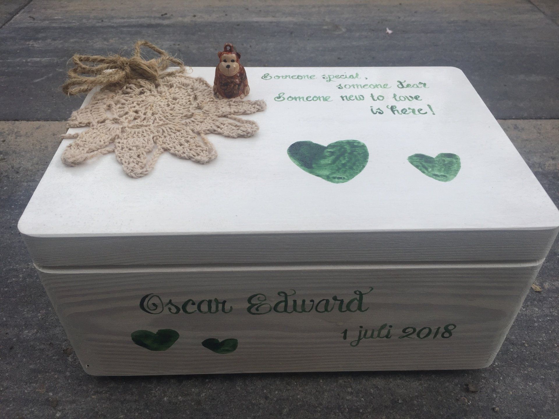 Witte gedenkdoos met groene bladeren, touw en de gegraveerde naam 