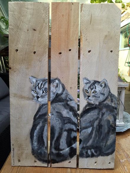 Geschilderde kat op drie houten planken, grijze cyperse kat met heldere ogen, zittend tegen een natuurlijke houten achtergrond.