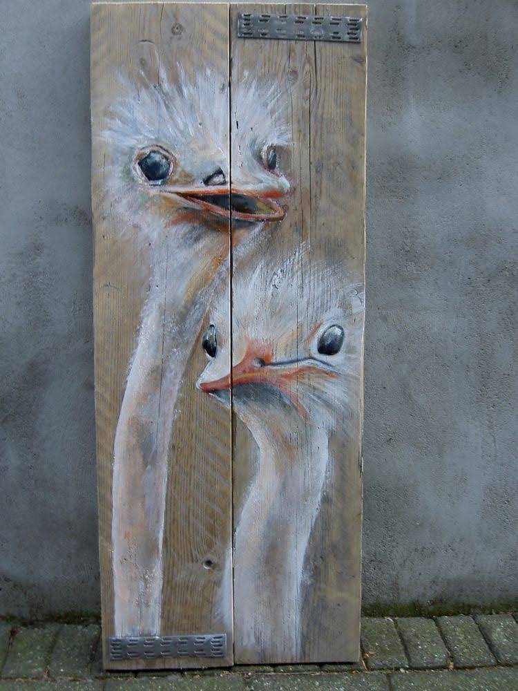 Twee gestileerde witte vogels geschilderd op een verweerd houten paneel tegen een betonnen muur.