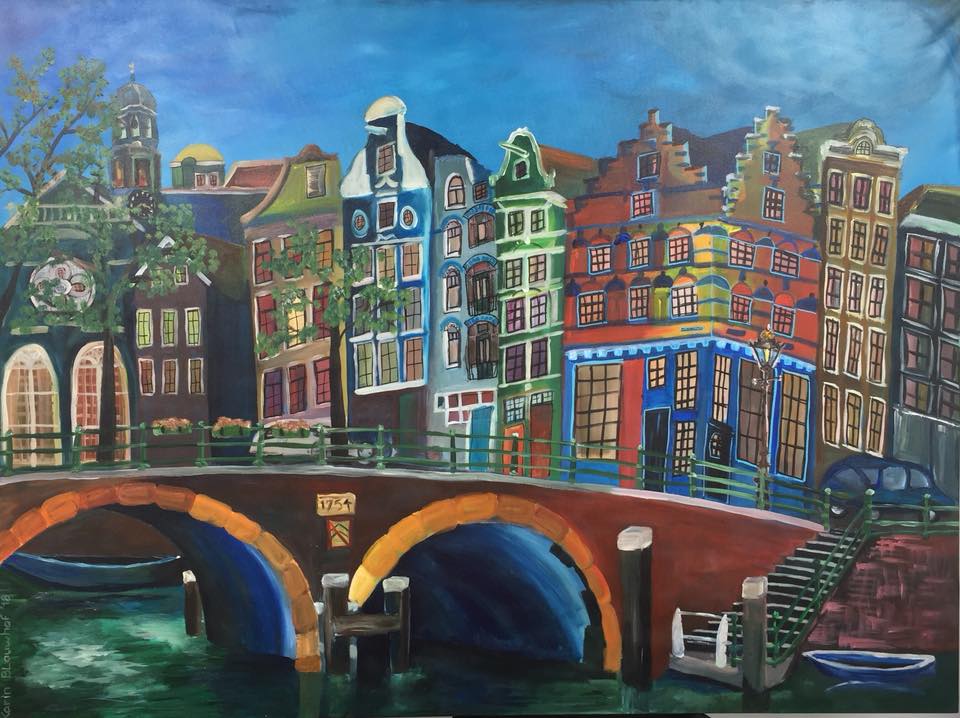 Kleurrijke grachtenpanden en een bakstenen brug die weerspiegeld worden in het kalme water onder een blauwe hemel.