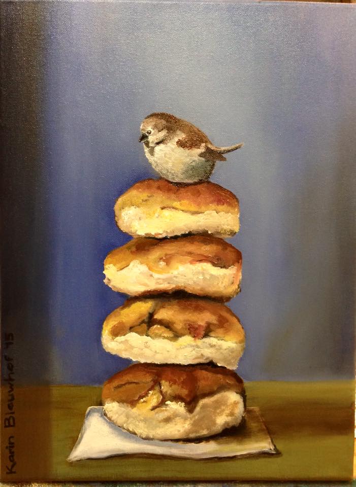 Een klein vogeltje zit bovenop een stapel van vier broodjes op een servet, tegen een blauwe achtergrond.