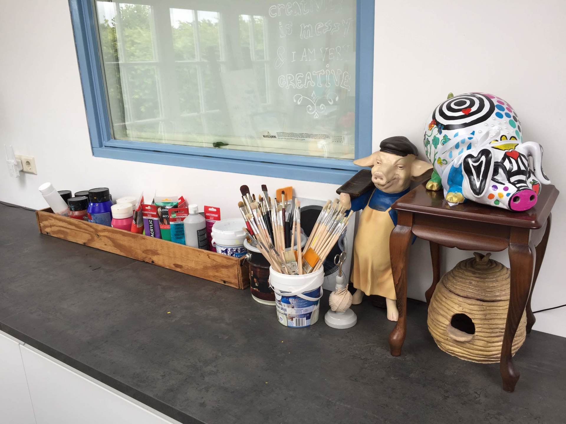 Vensterbankdecoratie met knutselspullen in bekertjes, kleine beeldjes en een kleurrijk versierde helm.