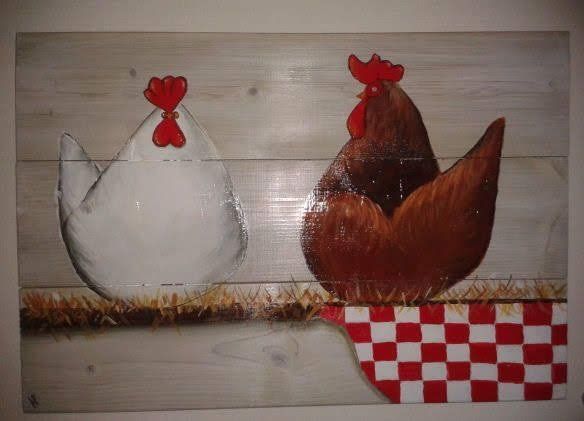 Twee geschilderde kippen op een houten bord, een witte en een bruine, met een rood-wit geblokt doek.