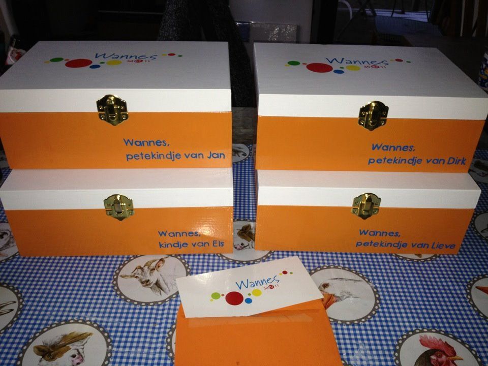 Op elkaar gestapelde oranje-witte geschenkdozen met een bijpassende kleinere doos op een tafelkleed met patroon.