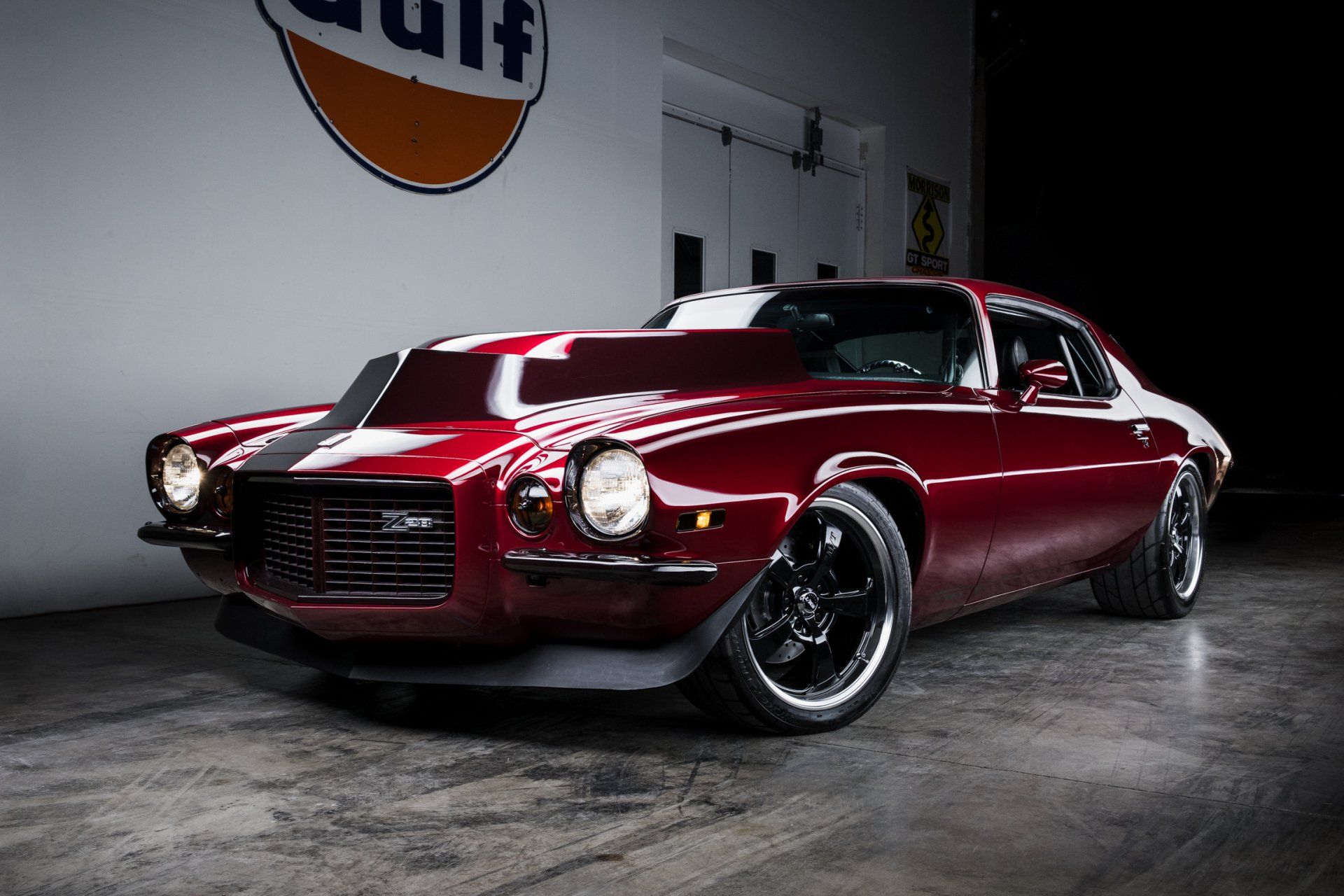 Maroon classic muscle car with white racing stripe, parked indoors under studio lighting