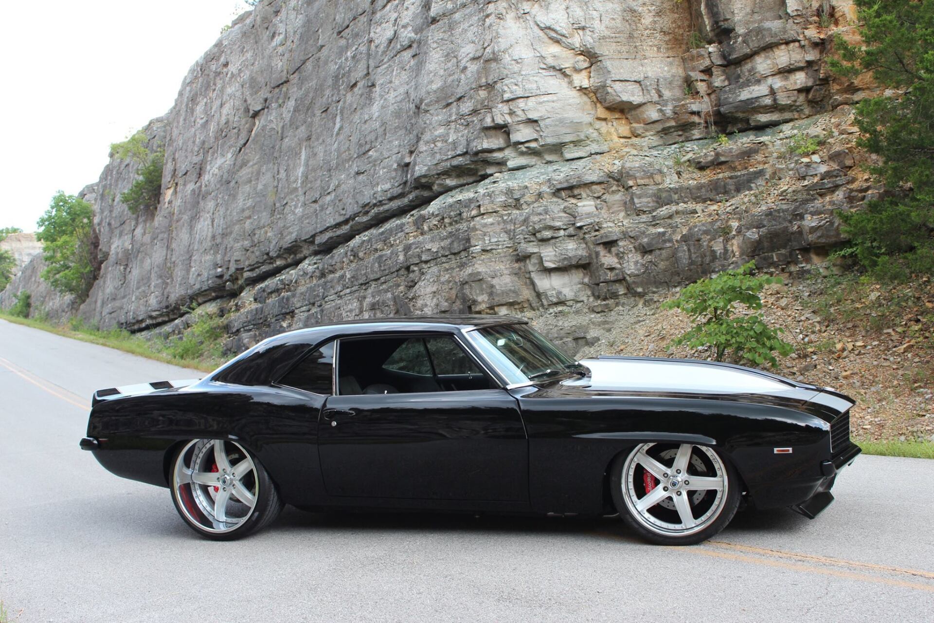 Black classic muscle car parked on a road beside a rocky cliff