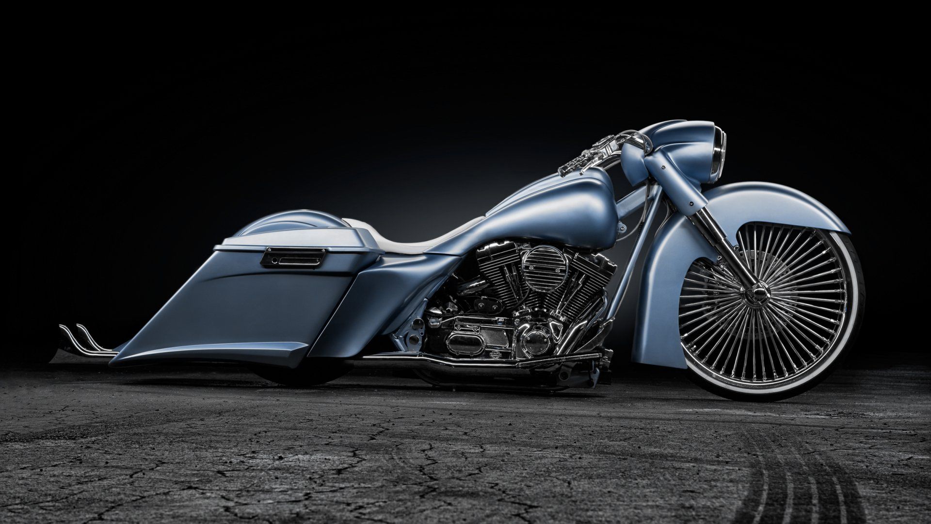 Custom metallic blue motorcycle with large front wheel, shown in side view on a dark studio background