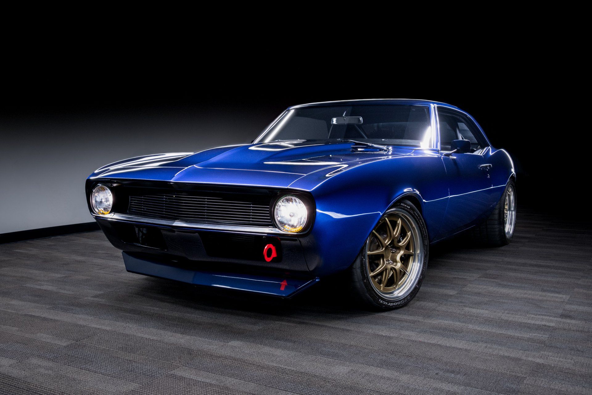 Blue classic sports car on display in a dark studio, front three-quarter view