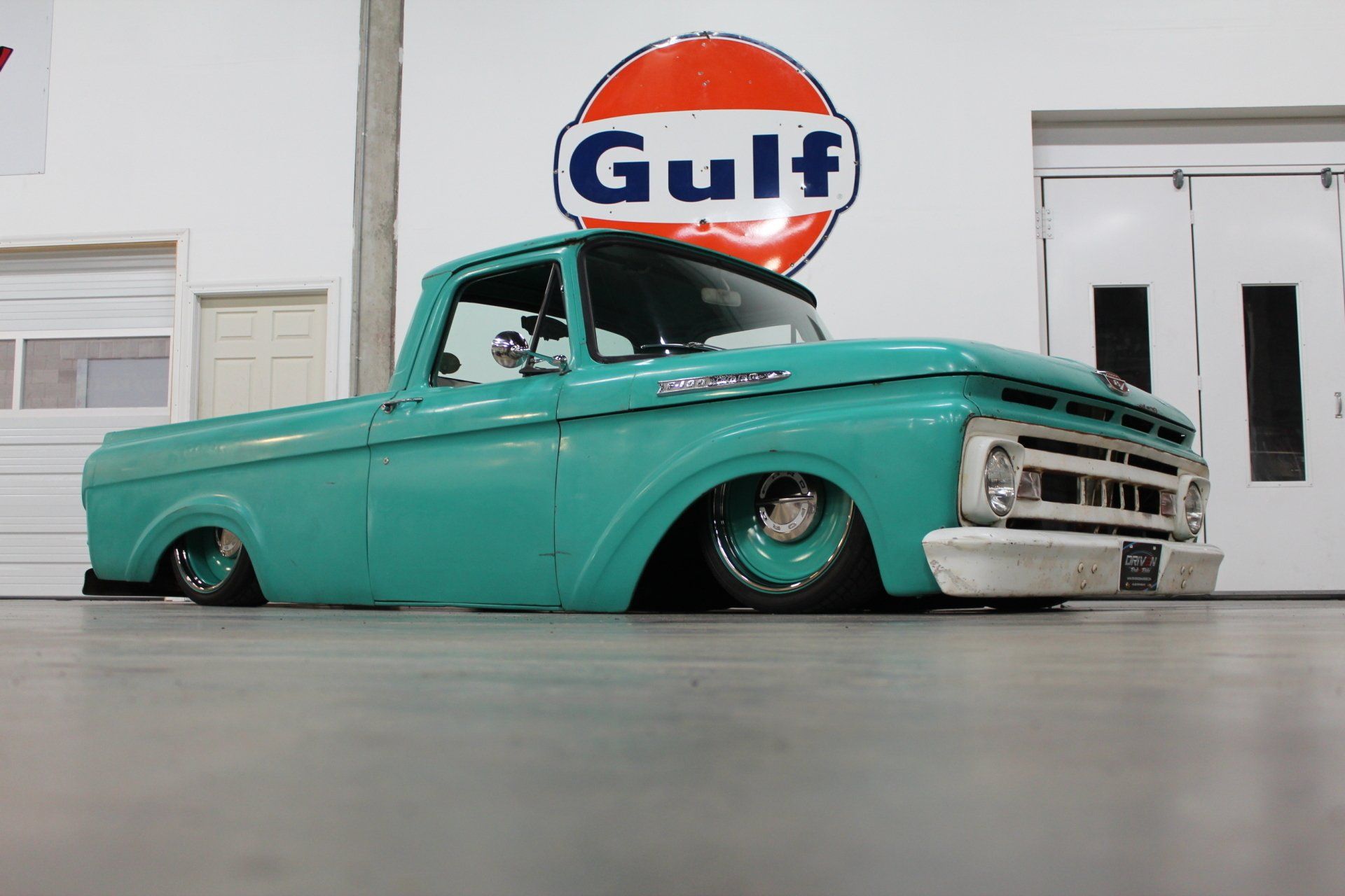 Turquoise lowered classic pickup truck indoors beneath a Gulf sign
