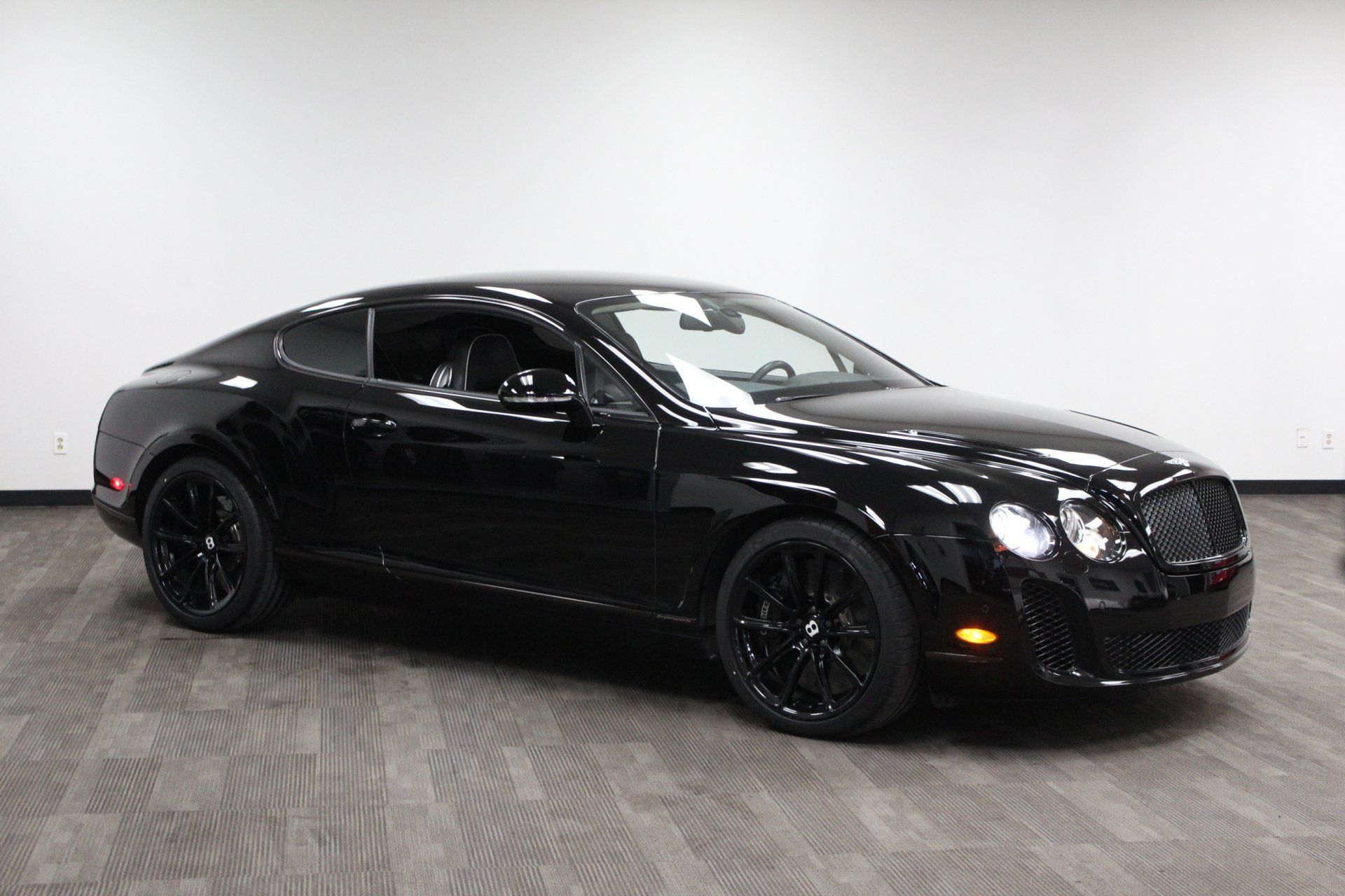 Black sports coupe parked indoors on a gray floor against a white backdrop