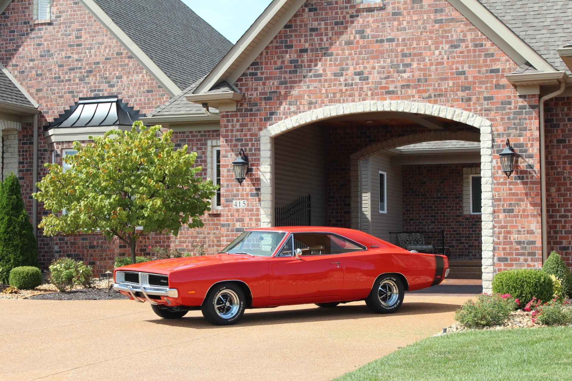 Red classic car parked in a brick driveway in front of a house with an arched entryway