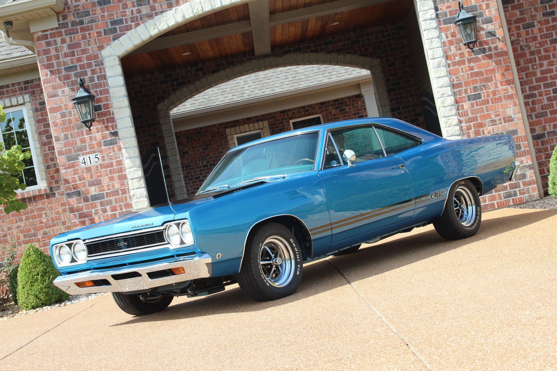 Blue classic car parked in front of a brick house garage