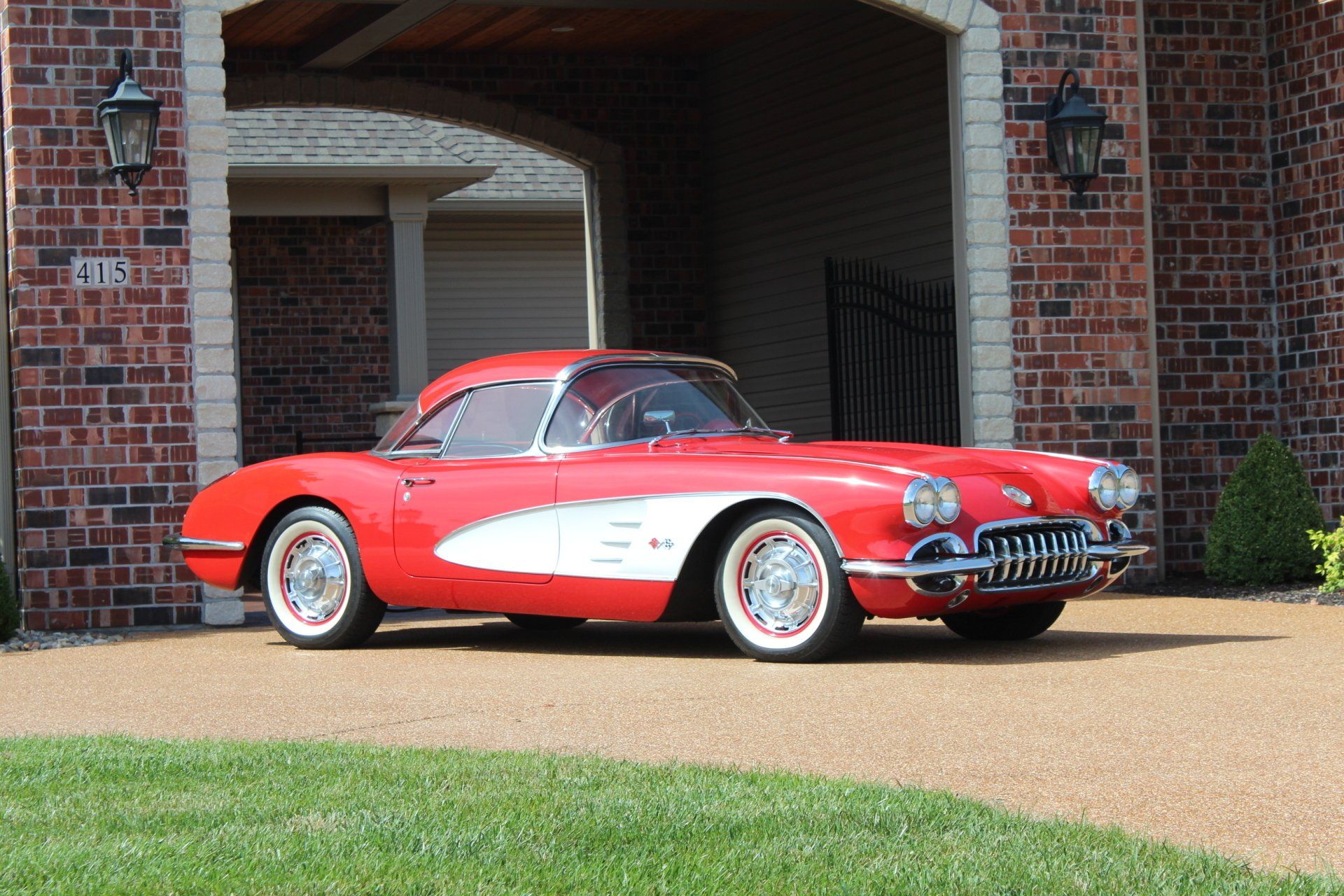 Red classic convertible sports car parked in a brick driveway beside a house