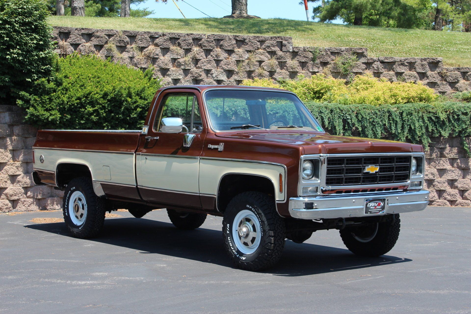 Two-tone classic Chevrolet pickup truck parked outdoors by a stone wall and greenery