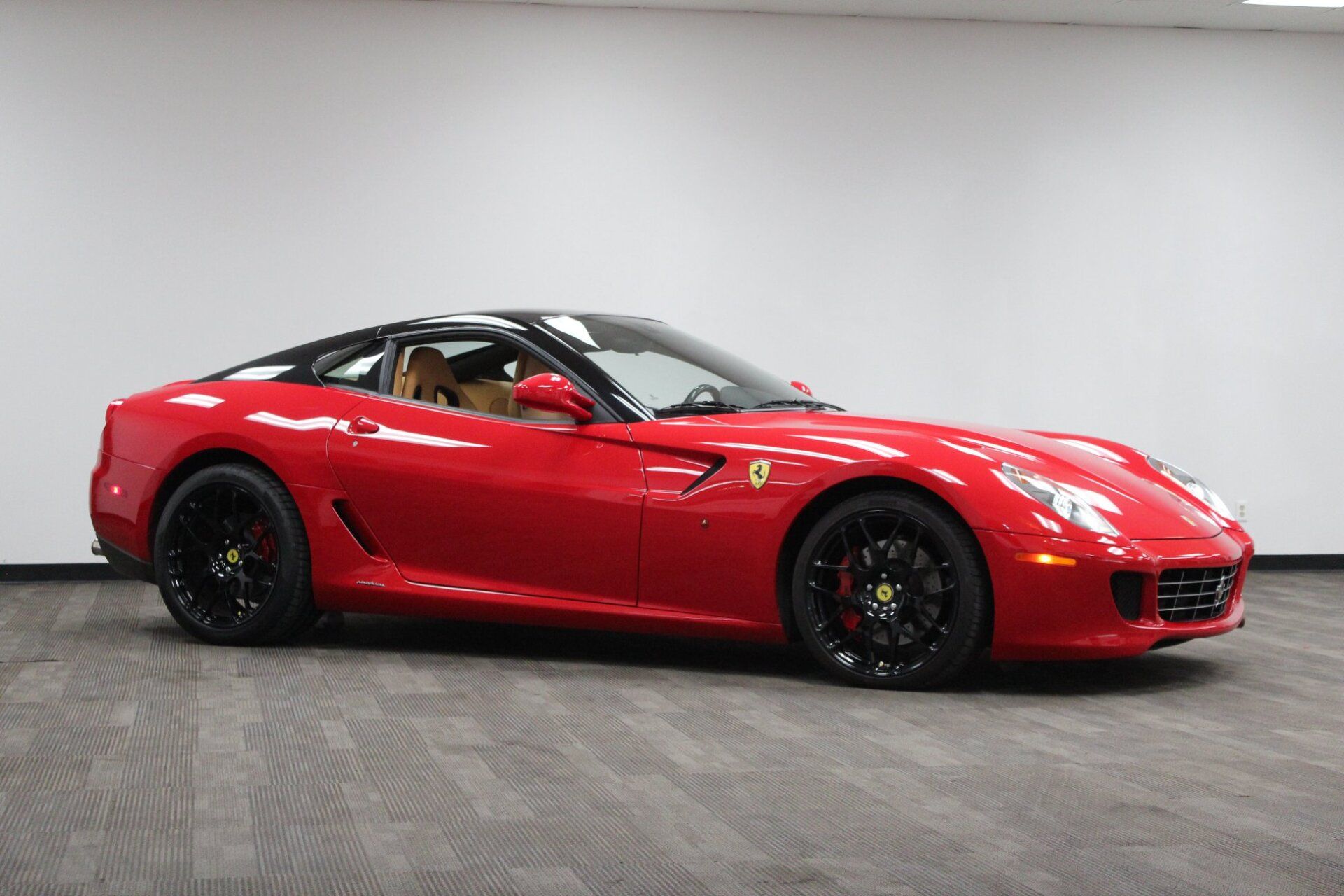 Red sports car in a studio, side view on a gray floor against a white wall.