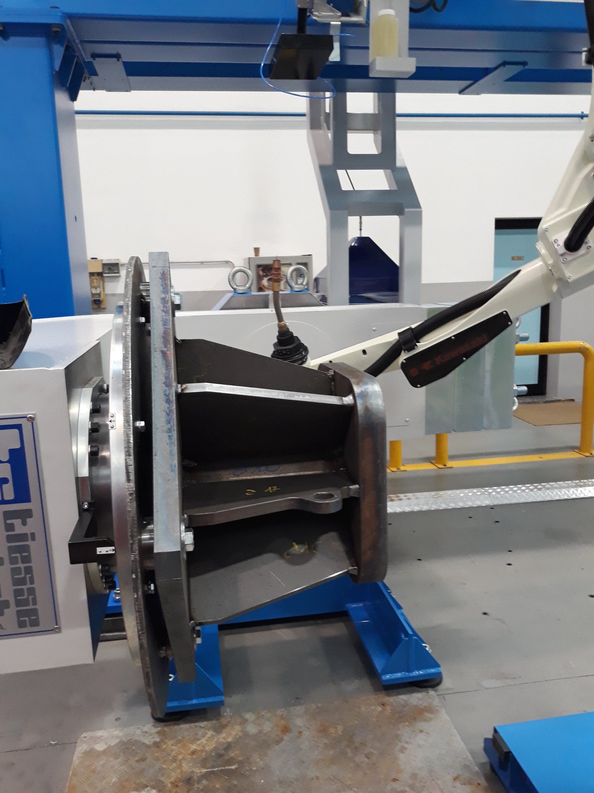 Un braccio robotico opera su un componente metallico fissato a un dispositivo rotante industriale all'interno di uno stabilimento di produzione.