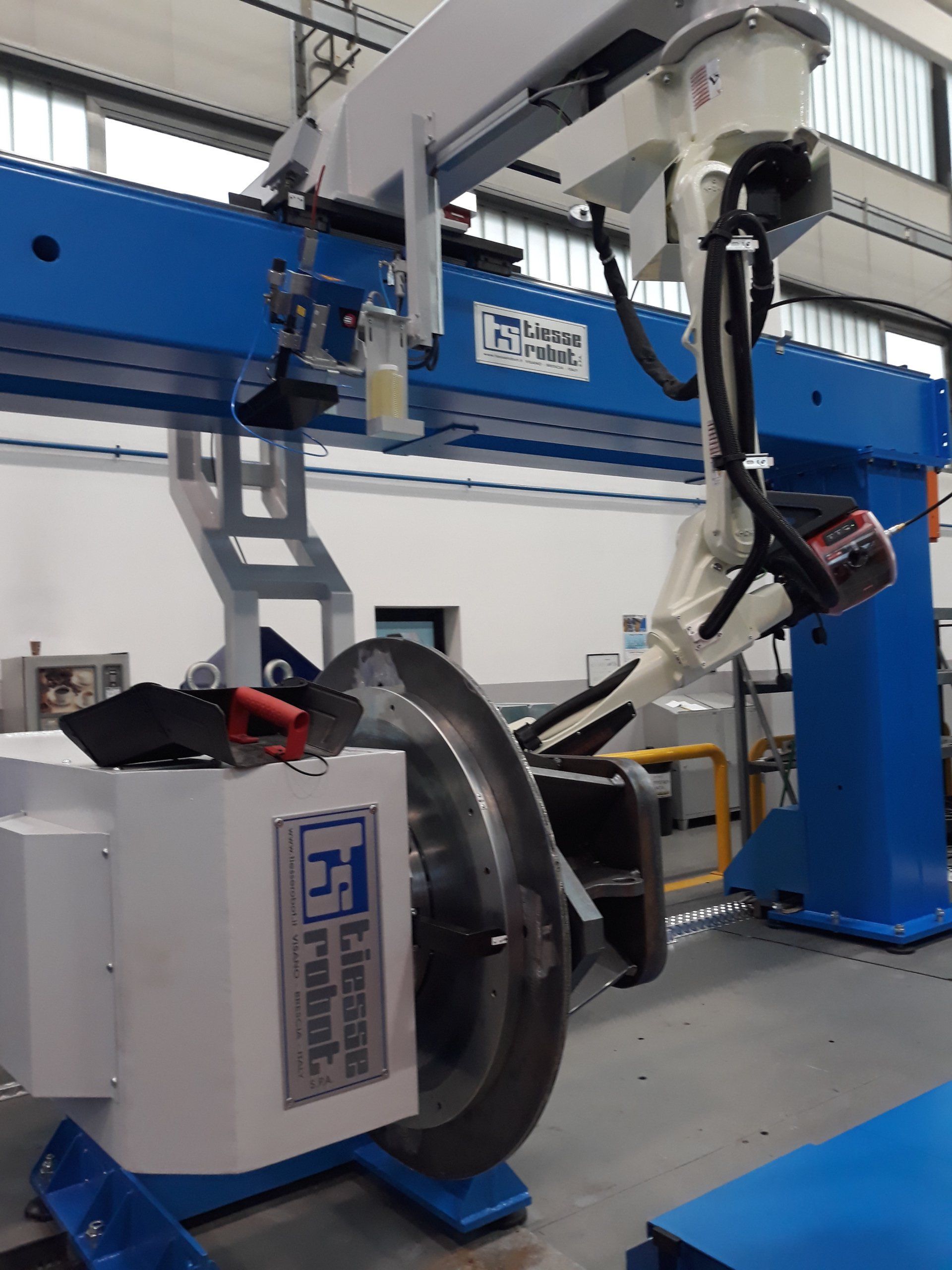 Un braccio robotico industriale Tiesse Robot esegue interventi di manutenzione su un componente metallico di una ruota in un ambiente di fabbrica.