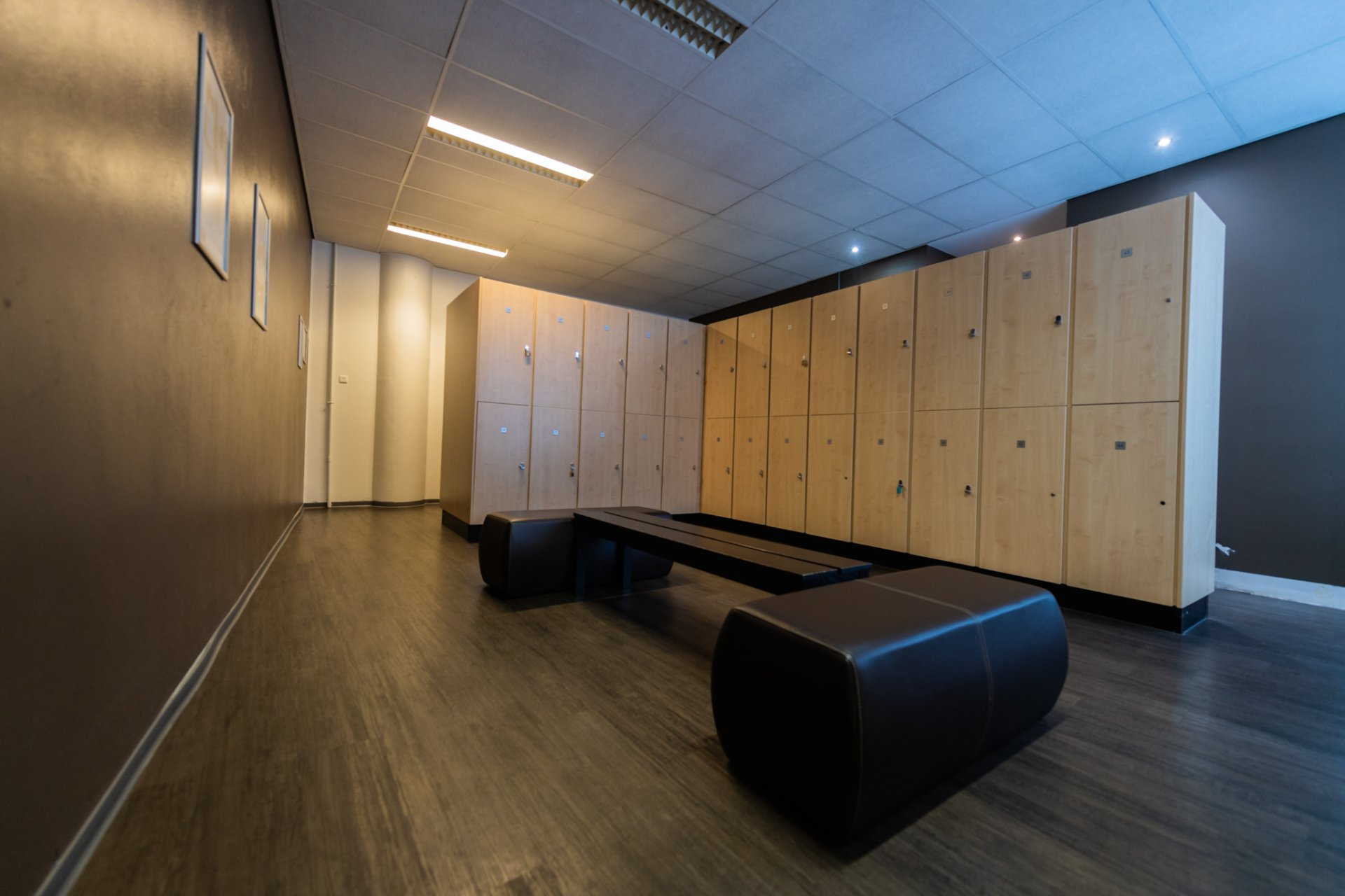 een kleedkamer met veel houten kluisjes en een bankje.
