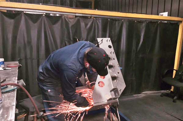 A man in a blue shirt is grinding a piece of metal